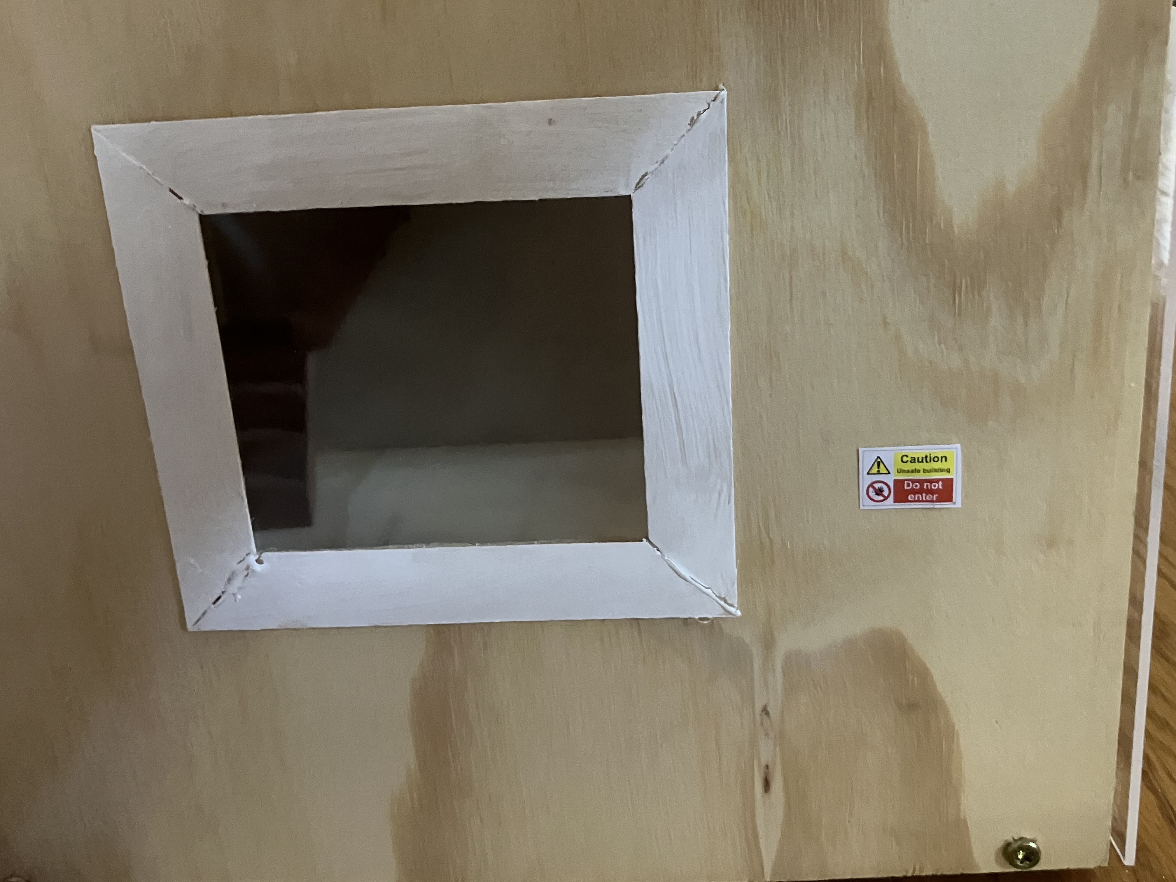 bottom windown of dollhouse with tiny sign reading &ldquo;Caution - Unsafe Building - Do Not Enter&rdquo;